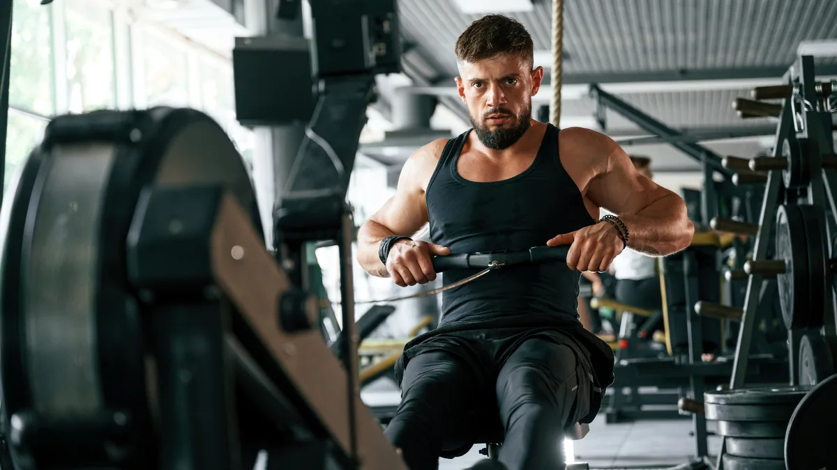 A man lifting a barbell in a well-lit gym, focused on steady progress.