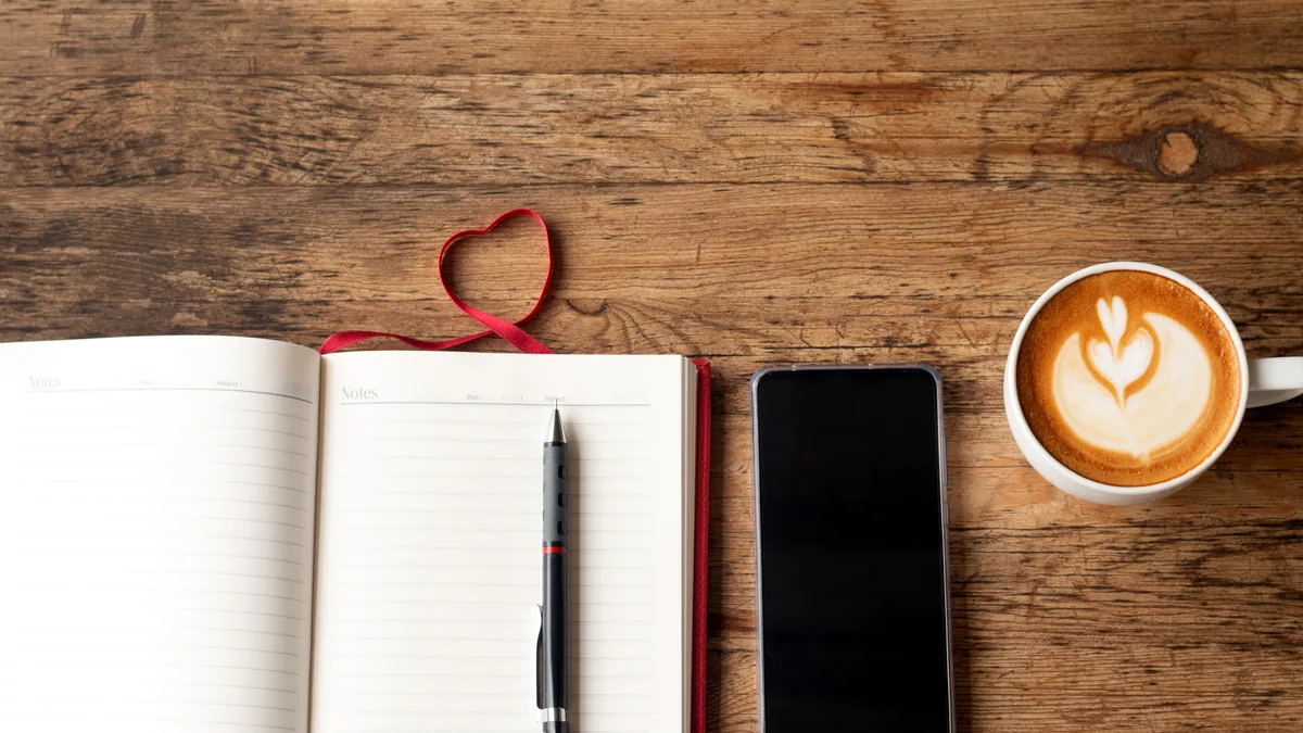 A steaming coffee cup beside a leather-bound journal on a sunlit desk.