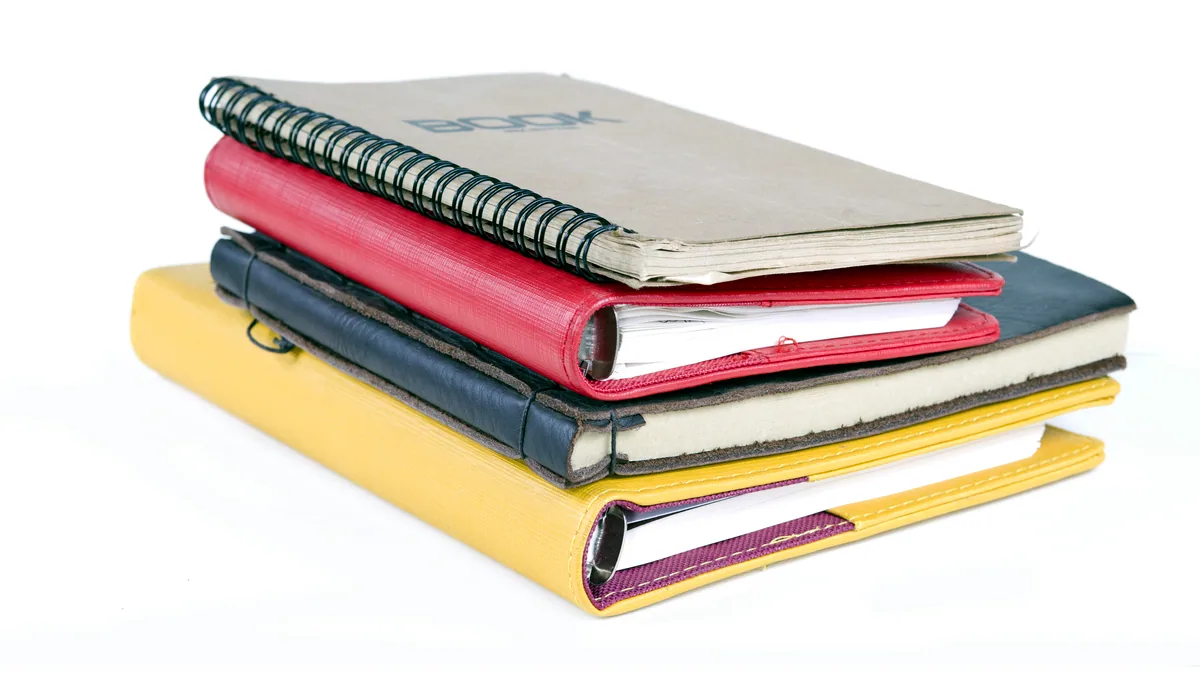 A tidy stack of hardcover books beside a blank notebook and a pencil.